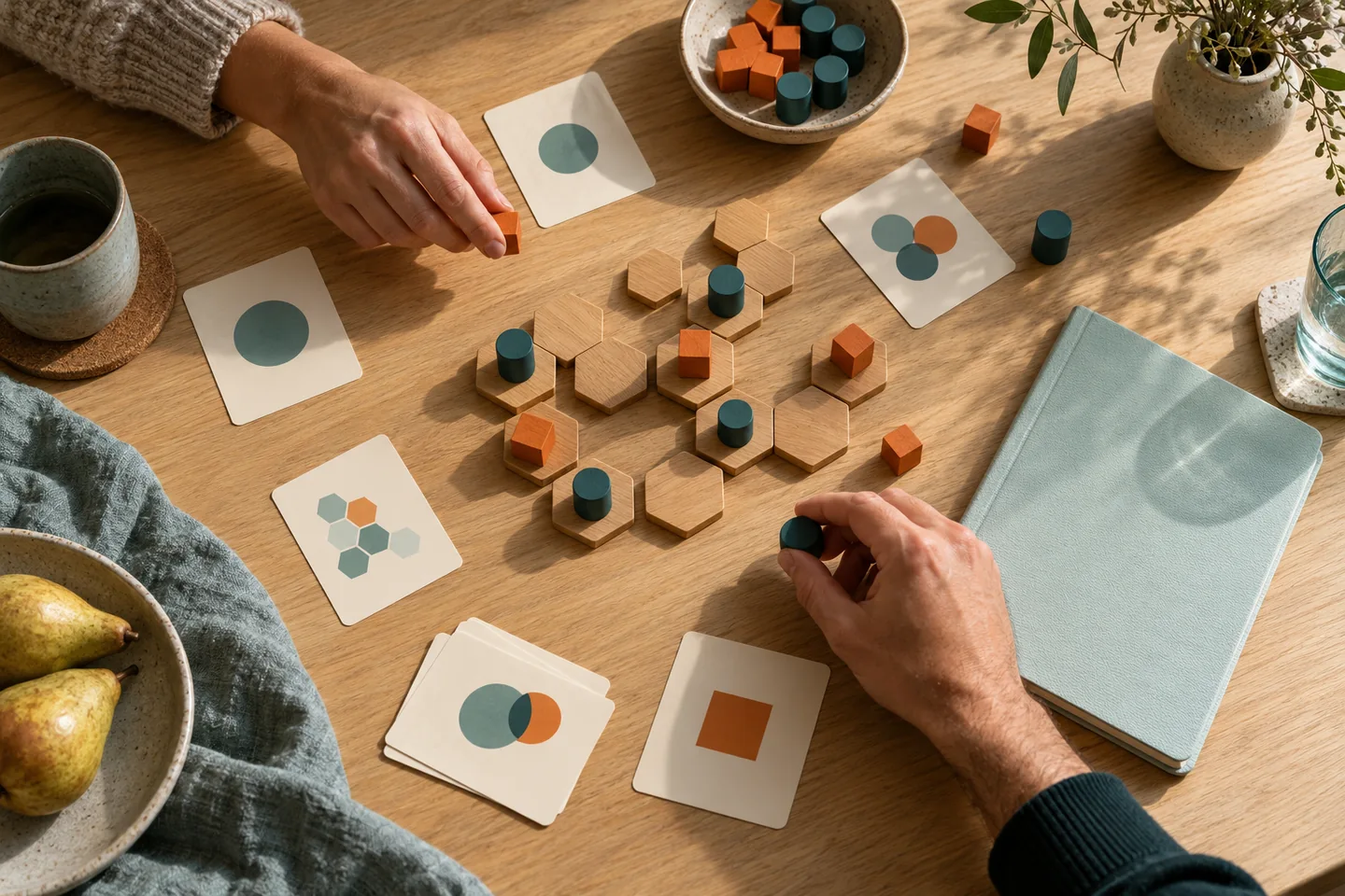 Hands considering an abstract game position with teal and orange pieces